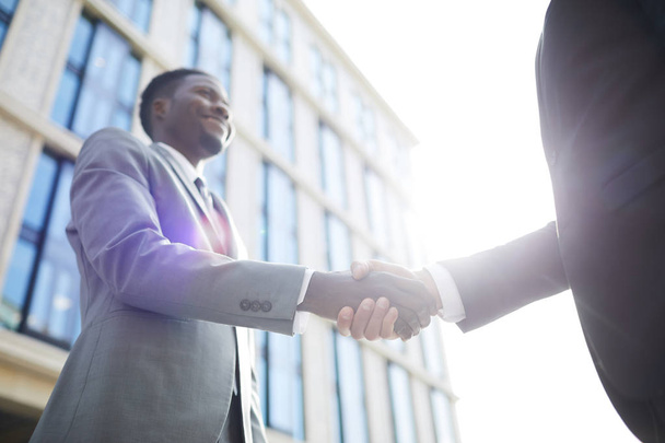 Close-up of multiethnic business people shaking hands while standing outdoors in city - 写真・画像