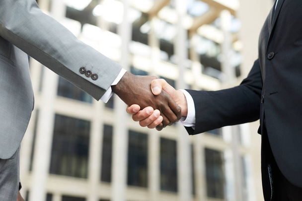 Крупный план многонациональных бизнесменов, пожимающих друг другу руки, стоя на улице в городе
 - Фото, изображение
