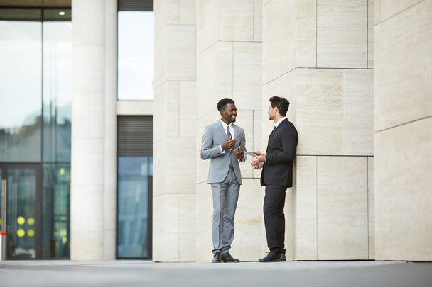 Two multiethnic coworkers standing and talking discussing working moments after meeting near the office building outdoors - Photo, Image