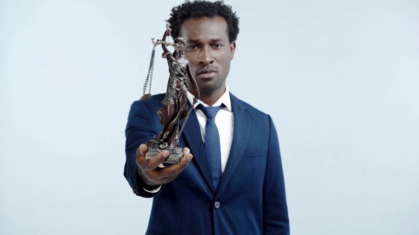 selbstbewusster afrikanisch-amerikanischer Anwalt zeigt themis Statue isoliert auf grau - Filmmaterial, Video
