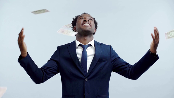灰色で隔絶されたお金の雨の下に立つ幸せなアメリカ人ビジネスマン - 映像、動画