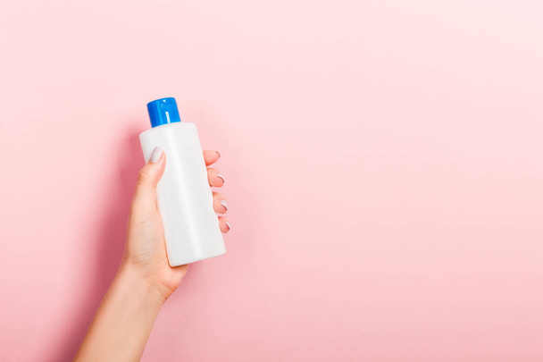 Female hand holding cream bottle of lotion isolated. Girl give tube cosmetic products on pink background - Valokuva, kuva