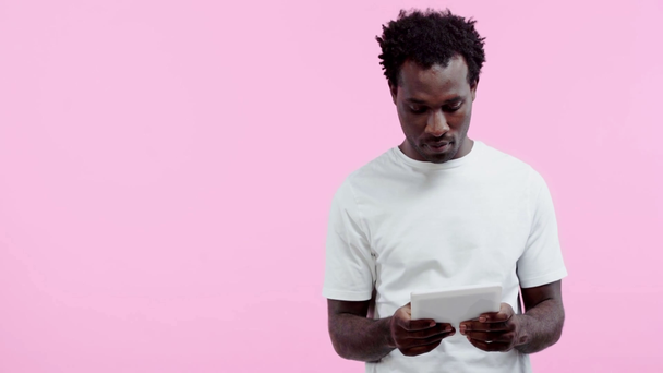 homem afro-americano atencioso usando tablet digital isolado em rosa
 - Filmagem, Vídeo