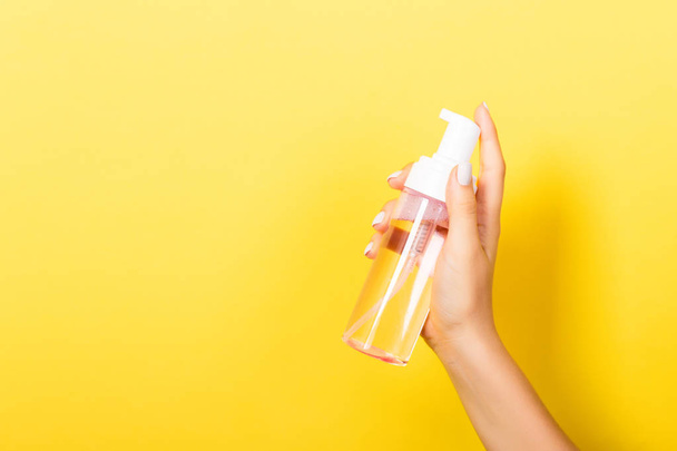 Kobieta ręka trzyma spray krem butelka balsam na białym tle. Dziewczyna daje produkty kosmetyczne na żółtym tle - Zdjęcie, obraz