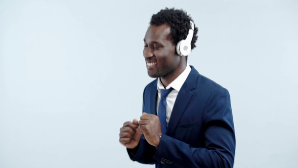 positive african american businessman dancing in headphones isolated on grey - Кадри, відео