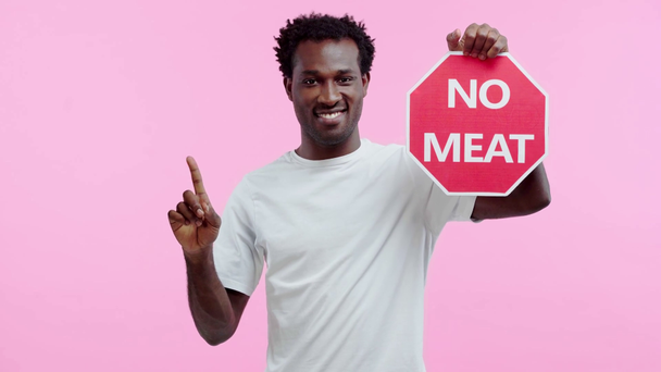 uśmiechnięty Afroamerykanin nie pokazuje żadnej karty mięsnej wyizolowanej na różowo - Materiał filmowy, wideo