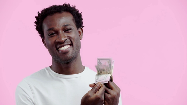 щасливий афроамериканський чоловік тримає доларові банкноти ізольовані на рожевому
 - Кадри, відео