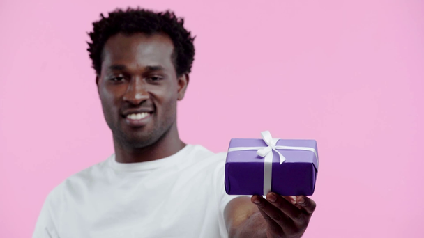 hombre afroamericano positivo que presenta la caja de regalo aislada en rosa
 - Imágenes, Vídeo