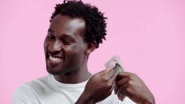 ピンクで孤立したドル紙幣を持っている幸せなアフリカ系アメリカ人男性は - 映像、動画