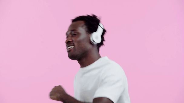 Χαρούμενος Αφροαμερικάνος που χορεύει με ακουστικά απομονωμένος σε ροζ - Πλάνα, βίντεο