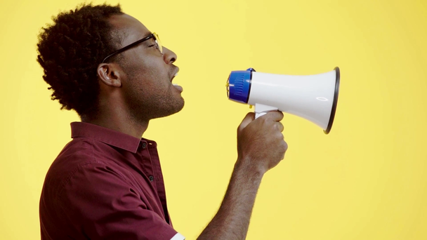 podrážděný africký Američan křičí do reproduktoru izolované na žluté - Záběry, video