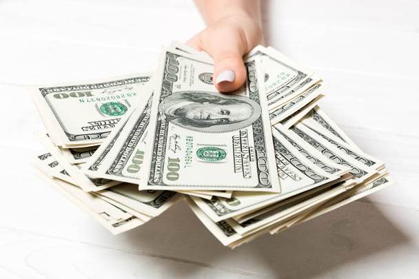 Eine weibliche Hand hält ein Bündel Hundert-Dollar-Banknoten auf hölzernem Hintergrund. Gehalts- und Lohnkonzept - Foto, Bild