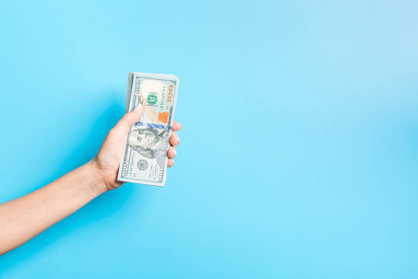 Dollar banknotes in female hand on blue background. Business concept - 写真・画像