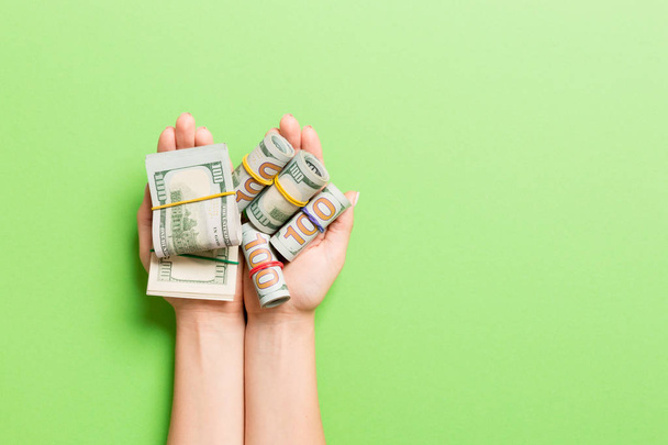 Vista superior de enrollado en billetes de dólares tubos en palmas femeninas sobre fondo colorido. Concepto de pobreza y deuda con espacio vacío para su diseño
 - Foto, imagen