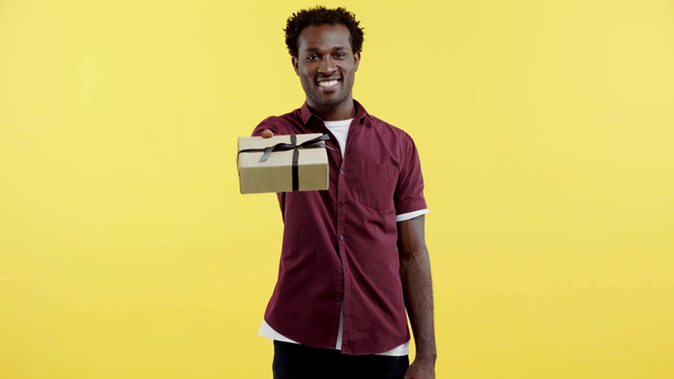positiive african american man presenting gift box isolated on yellow - Video, Çekim