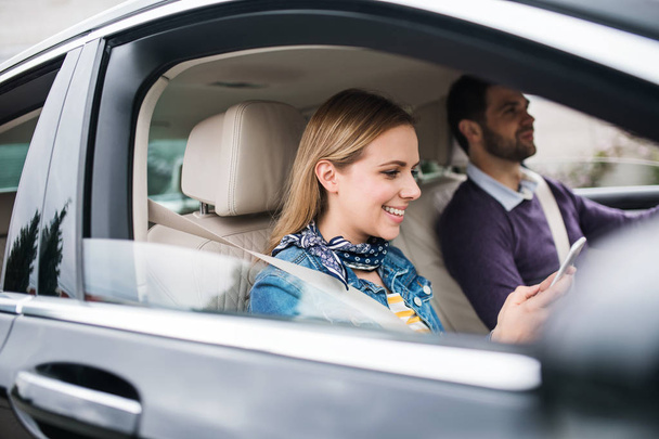 glückliches junges Paar sitzt mit Smartphone im Auto. - Foto, Bild
