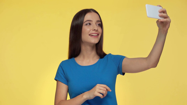 szczęśliwy dziewczyna biorąc selfie izolowane na żółty - Materiał filmowy, wideo