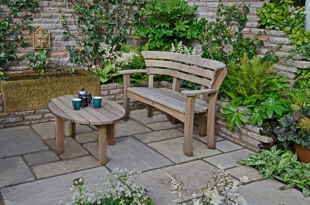 Close-up van een houten tuin zitje en tafel op een terras in een ommuurde tuin - Foto, afbeelding