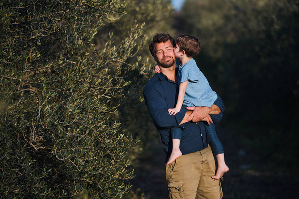 Vader met kleine dochter staande buiten door olijfboom, zoenen. - Foto, afbeelding
