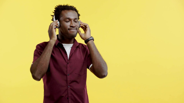happy african american man dancing in headphones isolated on yellow - Metraje, vídeo