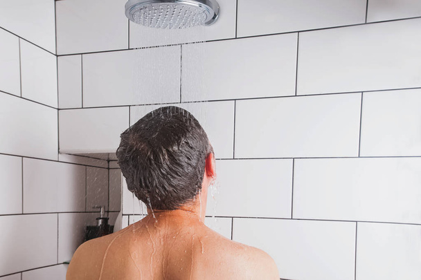 Young man taking shower in modern bathroom with white tile - Fotografie, Obrázek