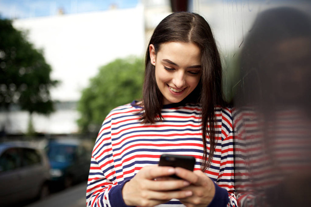 Портрет молодої жінки, яка посміхається і дивиться на мобільний телефон
 - Фото, зображення