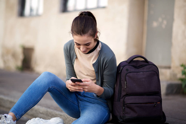 Portrait d'une étudiante heureuse assise à l'extérieur et regardant un téléphone portable
  - Photo, image