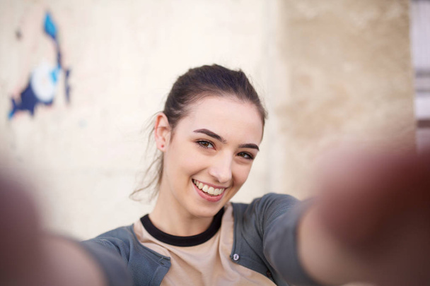 Portret szczęśliwej młodej kobiety biorąca selfie na ścianie - Zdjęcie, obraz