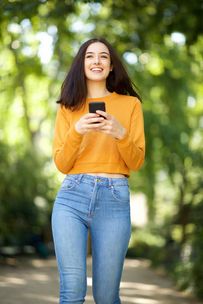 Portrait de jeune femme souriante marchant avec un téléphone portable dans le parc
 - Photo, image