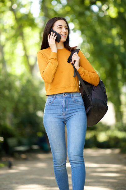 Portrait of college student walking through park with mobile phone and bag - Foto, immagini