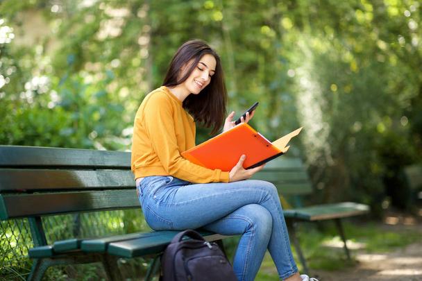 Portrait of college student sitting on park bench reading a book - Photo, Image
