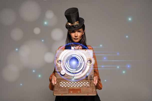steampunk woman in top hat with goggles showing vintage laptop with glowing digital illustration isolated on grey - Photo, Image