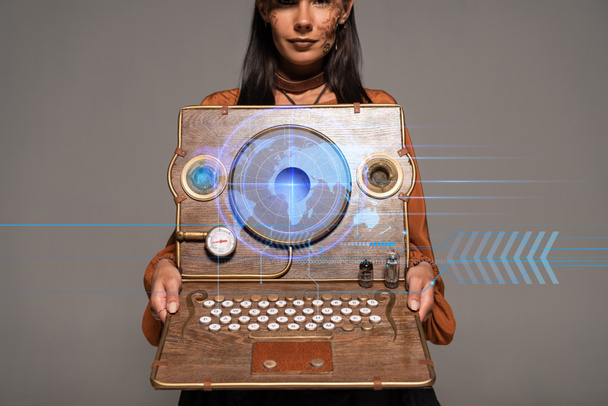 Ausgeschnittene Ansicht einer Steampunk-Frau mit Zylinder und Brille, die Vintage-Laptop mit digitaler Landkarte zeigt, isoliert auf grau - Foto, Bild