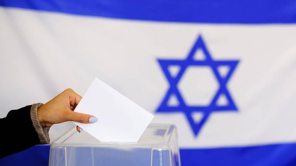 Seçim oyu konsepti için oy pusulasını elinde tutuyor. seçimler, oylarını sandık ta koyan kadının eli. Arka planda İsrail Bayrağı. - Fotoğraf, Görsel