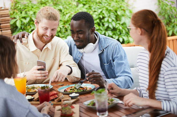Primer plano de los jóvenes sentados a la mesa comiendo ensalada de verduras y bebiendo jugo durante el almuerzo en la cafetería  - Foto, Imagen