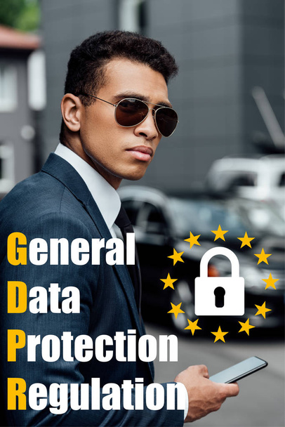 handsome and confident african american businessman in suit and sunglasses using smartphone with gdpr illustration - Photo, Image