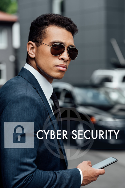 hombre de negocios afroamericano guapo y confiado en traje y gafas de sol usando teléfono inteligente con ilustración de seguridad en Internet
 - Foto, Imagen