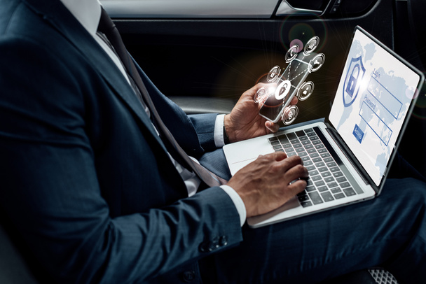 vue recadrée d'un homme d'affaires afro-américain utilisant un ordinateur portable et un smartphone dans une voiture avec une illustration de sécurité Internet
 - Photo, image