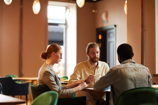 Groep van jonge zakenmensen hebben zakelijke bijeenkomst in coffeeshop ze zitten en bespreken toekomstige plannen in team - Foto, afbeelding