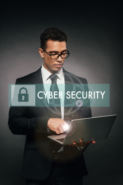 african american businessman using laptop on dark background with cyber security illustration - 写真・画像