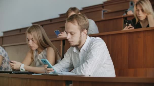 Многонациональная группа студентов с помощью лекций. Молодые люди используют социальные медиа во время учебы в университете
. - Кадры, видео