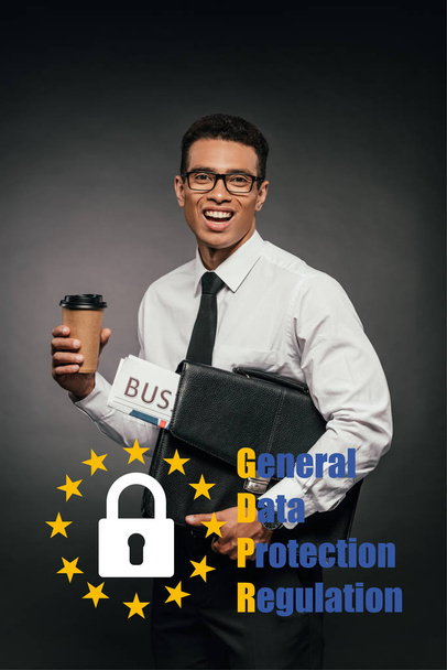 happy african american businessman holding newspaper, coffee to go and leather briefcase on dark background with gdpr illustration - Photo, Image