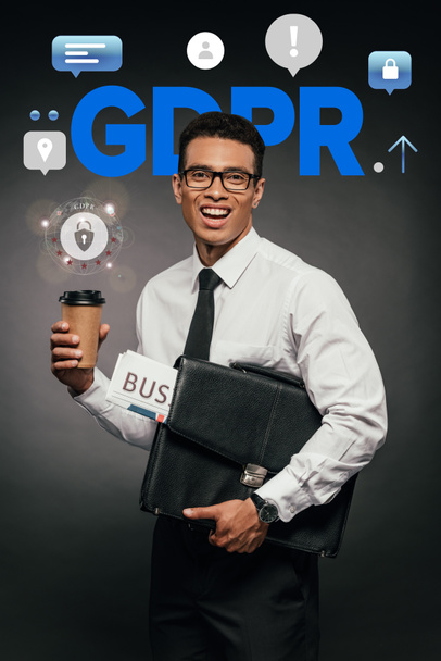 happy african american businessman holding newspaper, coffee to go and leather briefcase on dark background with gdpr illustration - Foto, immagini
