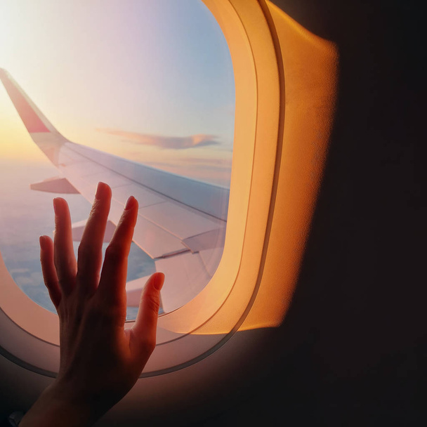 Womans hand touching a window glass on the plane in sunset light - Фото, изображение