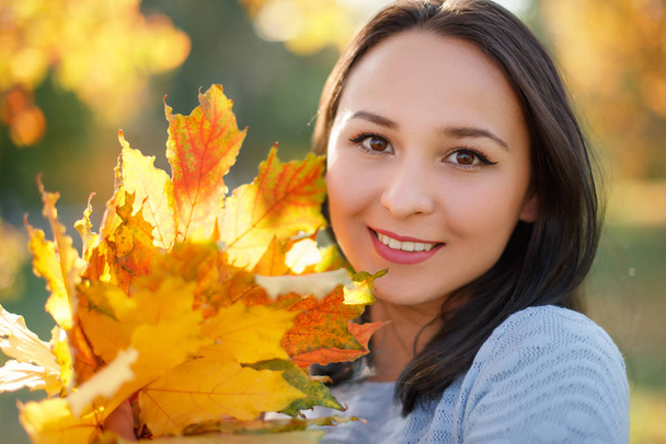 Portrait of smiling young woman with autumn leafs in front of foliage - Valokuva, kuva