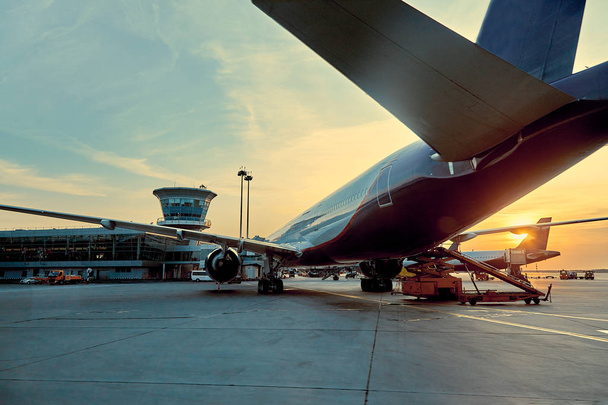 Moderni matkustaja lentokone pysäköity terminaalin rakennuksen portille lentokentän esiliina lähikuva lentokoneen osat suihkukone siipi ikkunat vaihde hinata traktori keskipäivän aurinko
 - Valokuva, kuva