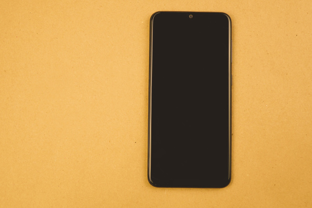 the black smartphone lies upright on a brown background - Foto, imagen