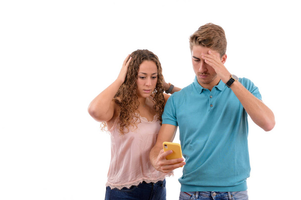 Jonge Kaukasische paar of broers ontvangen slecht nieuws op hun mobiele telefoon op zoek bezorgd of geschokt in witte achtergrond geïsoleerd, jongen gekleed in blauw shirt en roze meisje - Foto, afbeelding