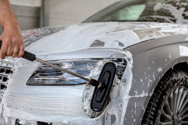 Front light of silver car washed in self serve carwash, man hand - Foto, imagen