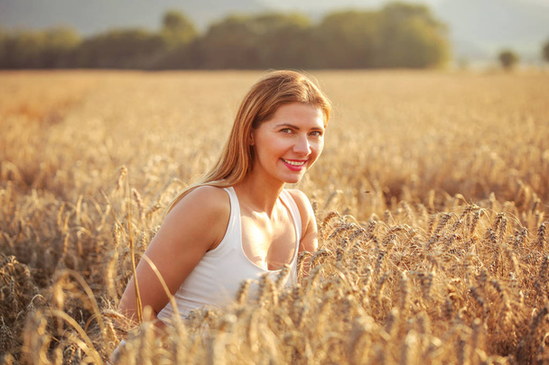 junge Frau im Weizenfeld von der Nachmittagssonne angestrahlt. - Foto, Bild